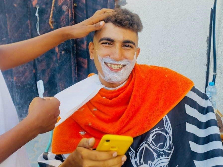 A man, getting a shave, smiles at the camera.