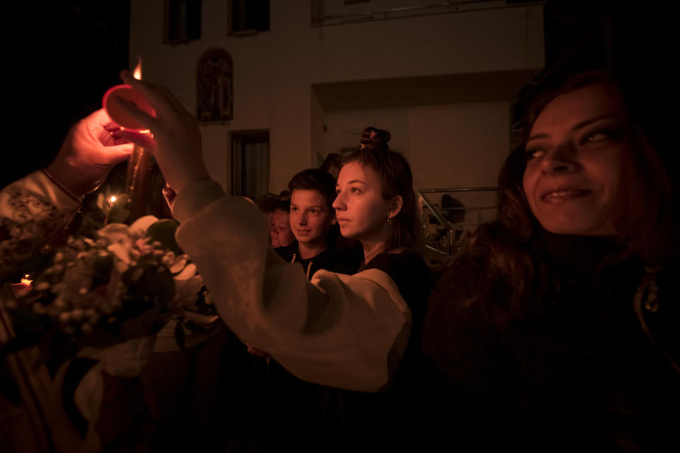 Ukrainian refugees receive holy light from an Orthodox priest during the Easter religious service at the Brancusi Parish Church in Bucharest, Romania, Sunday, April 24, 2022. The religious service was also attended by dozens of Ukrainian refugees living in a social center belonging to the church. (AP Photo/Andreea Alexandru)