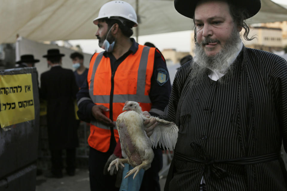 An ultra-Orthodox Jewish man carries a chicken to swing over his head as part of the Kaparot ritual in Jerusalem, Wednesday, Sept. 23, 2020. Observant Jews believe the ritual transfers one's sins from the past year into the chicken, and is performed before the Day of Atonement, Yom Kippur, the holiest day in the Jewish year, which takes place this year during a nationwide three-week lockdown to curb the spread of the coronavirus. A sanitation worker, center, stands ready to clean up the site, next to a yellow sign asking people to keep their distance. (AP Photo/Maya Alleruzzo)