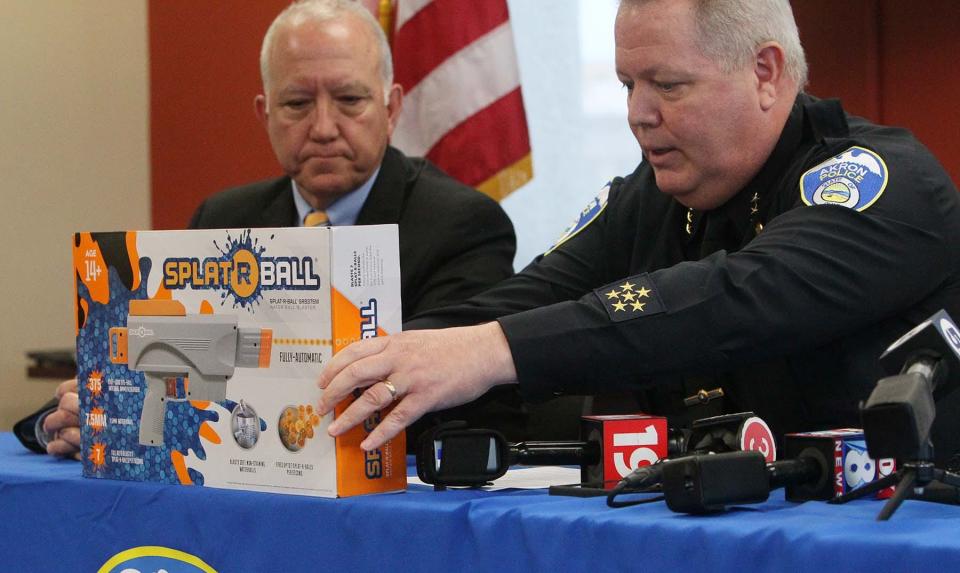 Akron Police Department Chief Stephen Mylett, right, seated next to Akron Mayor Dan Horrigan, shows a box containing a SplatRBall toy gun Splat-R-Ball during a press conference Wednesday at the police department.