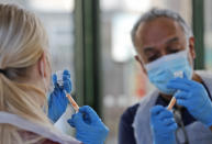 FILE - In this Friday, Feb. 5, 2021 file photo Doctor Anil Mehta and Apprentice Nursing Associate Ellie Bull prepare syringes with doses of the AstraZeneca vaccine at the Welcome Centre in Ilford, east London. Thanks to an efficient vaccine roll out program and high uptake rates, Britain is finally saying goodbye to months of tough lockdown restrictions. From Monday May 17, 2021, all restaurants and bars can fully reopen, as can hotels, cinemas, theatres and museums, and for the first time since March 2020, Britons can hug friends and family and meet up inside other people's houses. (AP Photo/Frank Augstein)