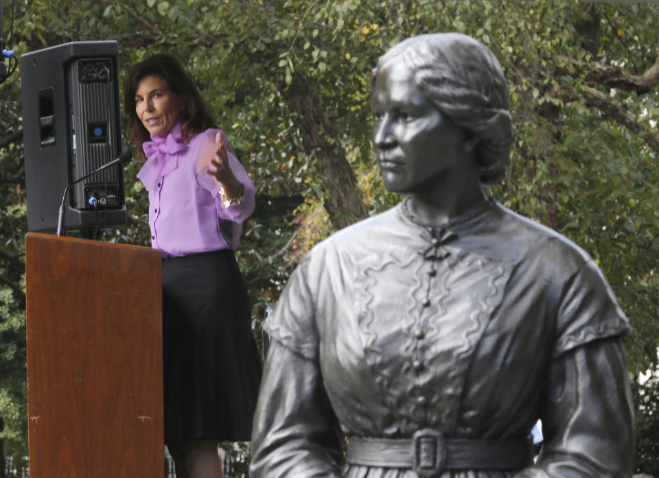 Former Virginia first lady Susan Allen gestures toward the statue of Elizabeth Keckly, seamstress and confidante to Mary Todd Lincoln, one of the seven statues unveiled at the dedication of the Virginia Women's Monument inside Capitol Square in Richmond, Va. Monday, Oct. 14, 2019. (Bob Brown/Richmond Times-Dispatch via AP)