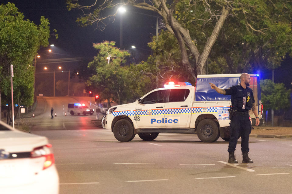 A police officer stands in front of a patrol car and points at the intersection of Stuart Highway and McMinn Street. Source: AAP