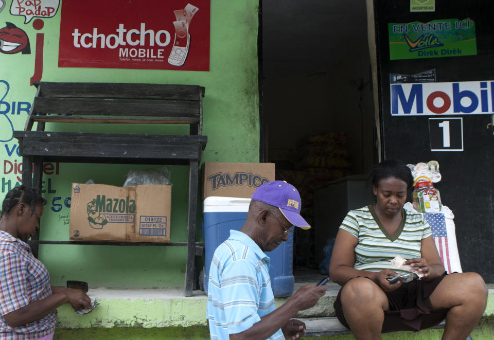 In this June 1, 2012 photo, a vendor of Digicel's Tchotcho Mobile services, right, makes a transfer for a client in front of her shop in Port-au-Prince, Haiti. Aid agencies trying to remake Haiti after a catastrophic earthquake are promoting a new way to bypass banks altogether: easy money transfers by cell phone. The plan lets people save and move money in mobile phone accounts and quickly withdraw it at a network of retail stores around the country. (AP Photo/Dieu Nalio Chery)