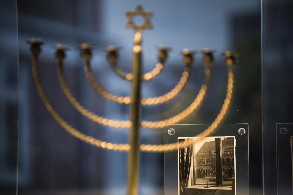 A photo showing the Hanukkah menorah belonging to the Posner family from Kiel, with a large swastika flag hanging from the facade of a building opposite, is part of an exhibition with items from Israel's Yad Vashem Holocaust memorial in the German parliament Bundestag in Berlin, Germany, Monday, Jan. 23, 2023. An exhibition marking the 70th anniversary of Israel's Yad Vashem Holocaust memorial brings back to Germany a diverse set of everyday objects that Jews took with them when they fled the Nazis. (AP Photo/Markus Schreiber)