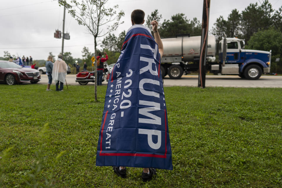 Bob Goes, of Windbur, Pa., with is 4-year-old son Emmett atop his shoulders, wears a "Trump 2020 Make America Great Again" flag as a cape near the entrance of the Flight 93 National Memorial during a memorial service attended by President Donald Trump in Shanksville, Pa., Friday, Sept. 11, 2020. (AP Photo/Carolyn Kaster)