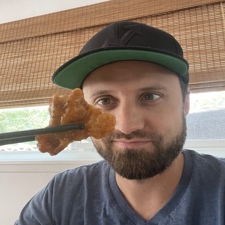 Andy Golder holding a piece of orange chicken with chopsticks.