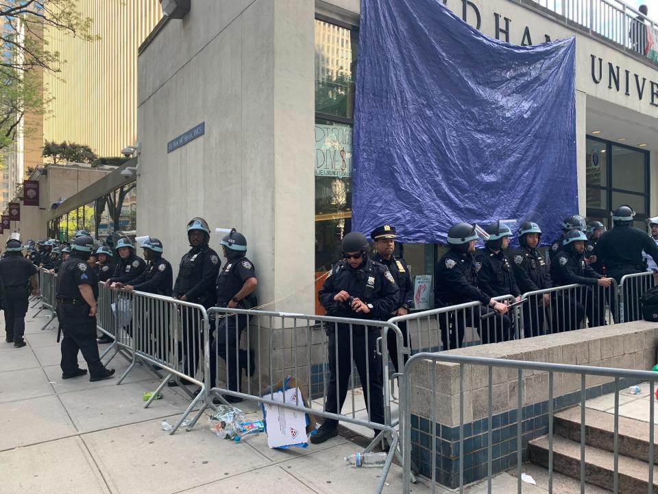 About 20 officers stand between a barricade and the front of a Fordham building.