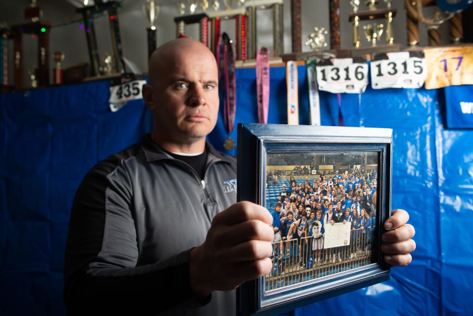Damon Parker holds a photograph from the boys wrestling 2019 season Wednesday in his shop in Auburn. The picture isn't from a championship but a group photo of all the individual wrestlers with their families.