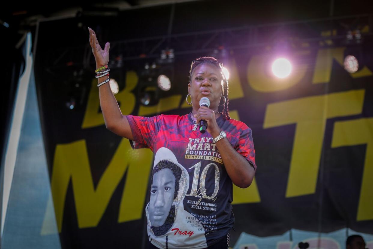 A woman in a multi-colored shirt speaks into a microphone on a stage.