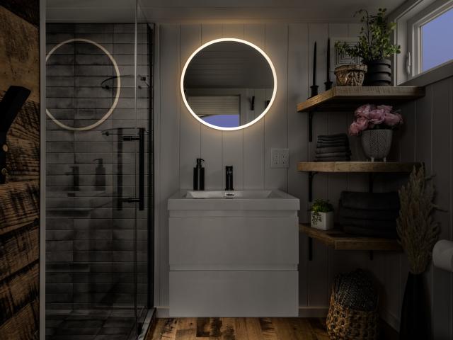 a dark bathroom with a lit up round mirror