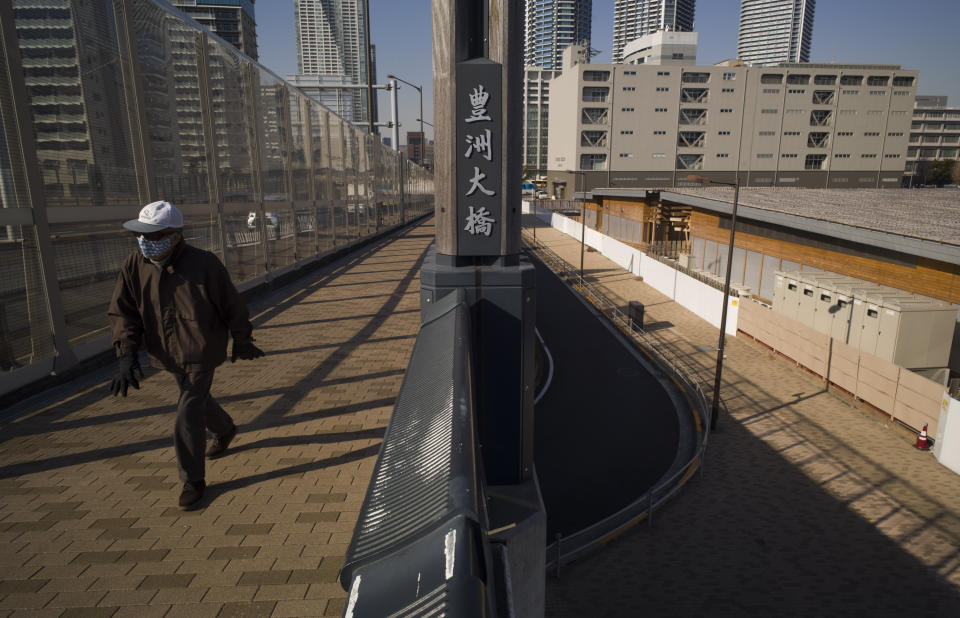 A man walks on a bridge past a closed building complex, right, built to be used for the athletes' village during the rescheduled Tokyo Olympics, in Tokyo on Thursday, Jan. 21, 2021. The postponed Tokyo Olympics are to open in just six months. Local organizers and the International Olympic Committee say they will go ahead on July 23. But it’s still unclear how this will happen with virus cases surging in Tokyo and elsewhere around the globe. (AP Photo/Hiro Komae)