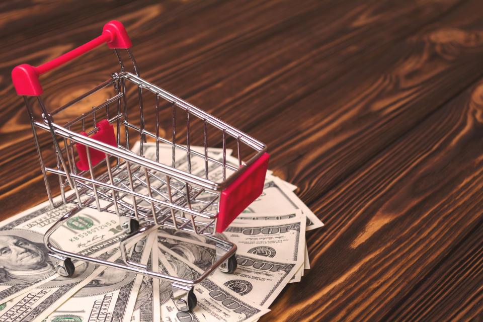 A miniature shopping cart with cash underneath standing on a wooden floor.