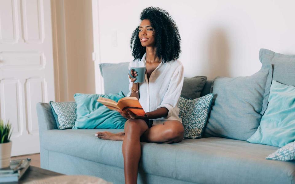 Young woman reading a book at home while drinking coffee