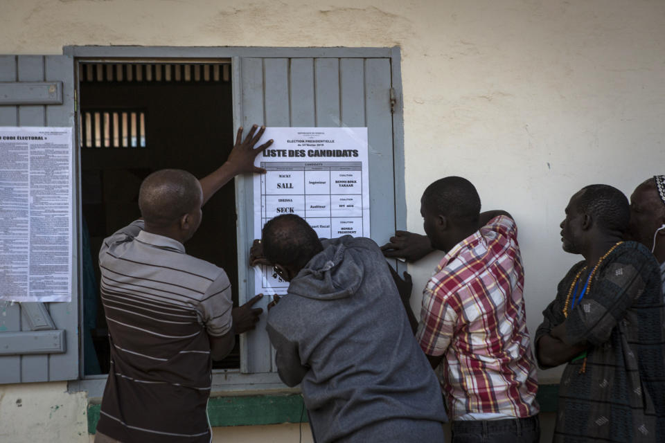 Senegalese men post a list of presidential candidates outside a polling station in Dakar, Senegal Sunday Feb. 24, 2019. Voters are choosing whether to give President Macky Sall a second term in office as he faces four challengers.(AP Photo/Jane Hahn)