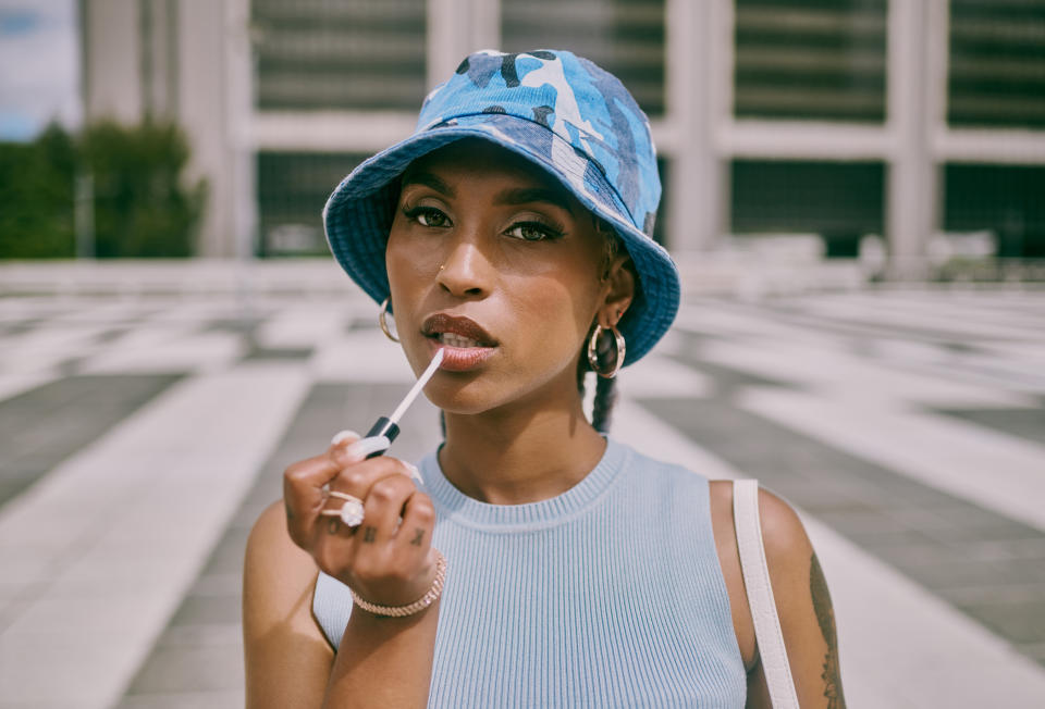 Woman in a sleeveless top and bucket hat applying lip gloss outdoors