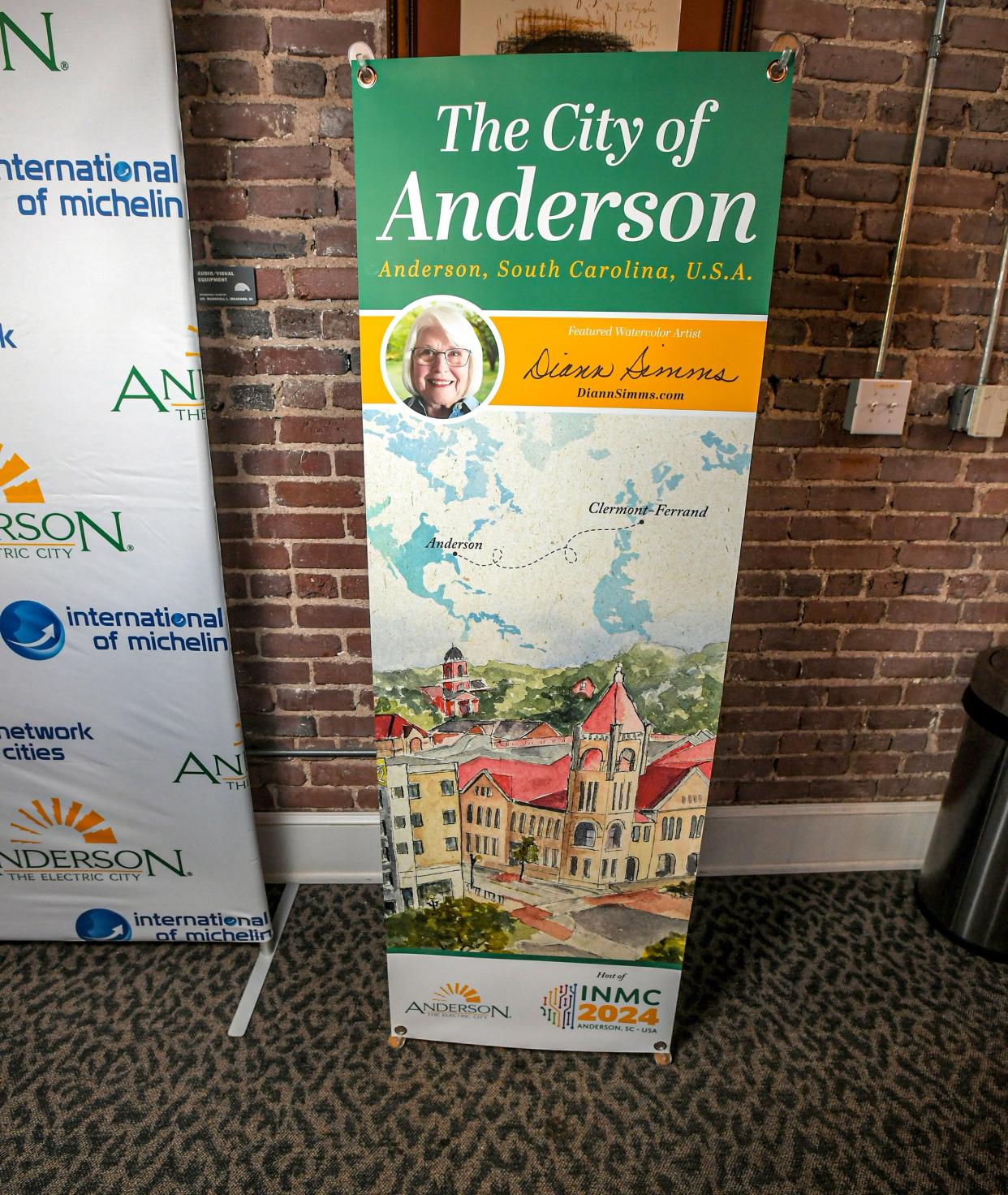 A poster showing City of Clermont-Farrand, France and City of Anderson, during The International Network of Michelin Cities Conference announcement by Mayor Terence Roberts, at the Anderson Arts Center Tuesday, October 10, 2023. Anderson was selected to host the fourth Conference of the International Network of Michelin Cities on Feb 14, with a "Drivers of Economic Development" theme.