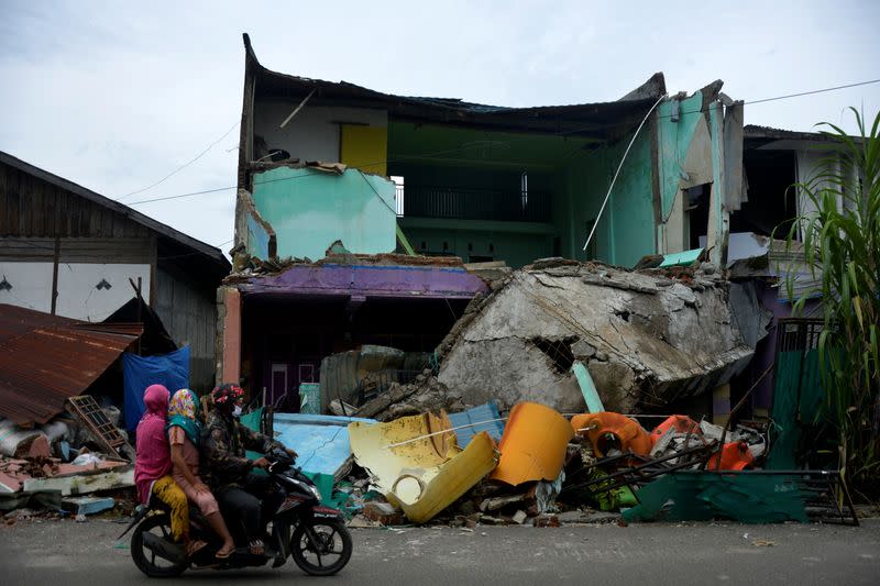 Locals ride a motorbike past a collapsed house following an earthquake in Mamuju