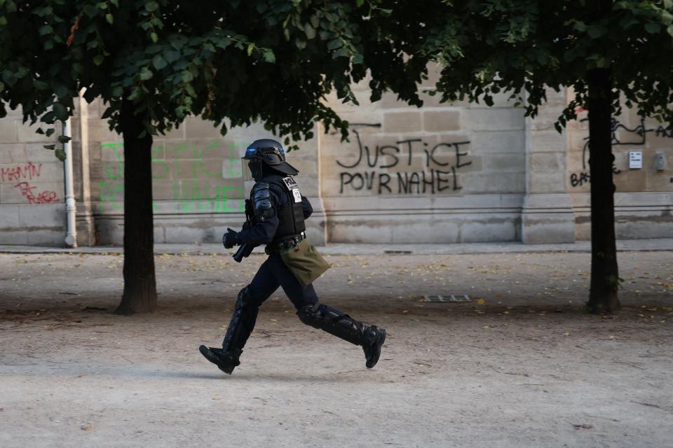 A CRS riot police officer runs past graffiti reading 