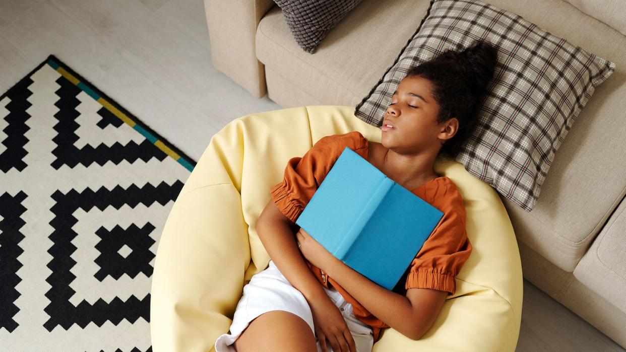 young girl sleeping on bean bag with book