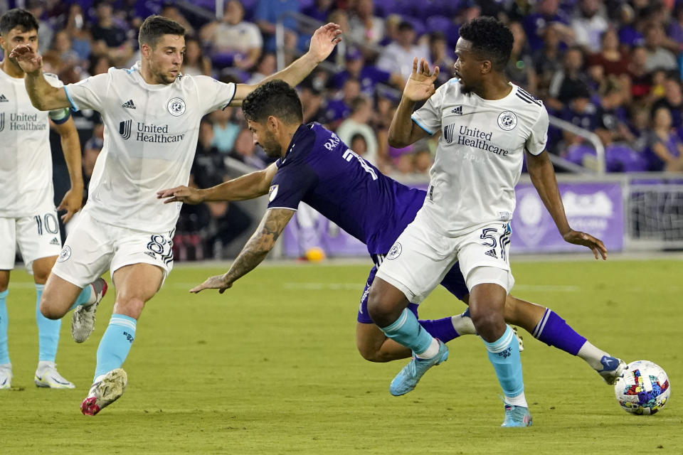 Orlando City's Alexandre Pato (7) falls as he tries to move the ball between New England Revolution's Wilfrid Kaptoum (5) and Matt Polster, left, during the second half of an MLS soccer match Saturday, Aug. 6, 2022, in Orlando, Fla. (AP Photo/John Raoux)