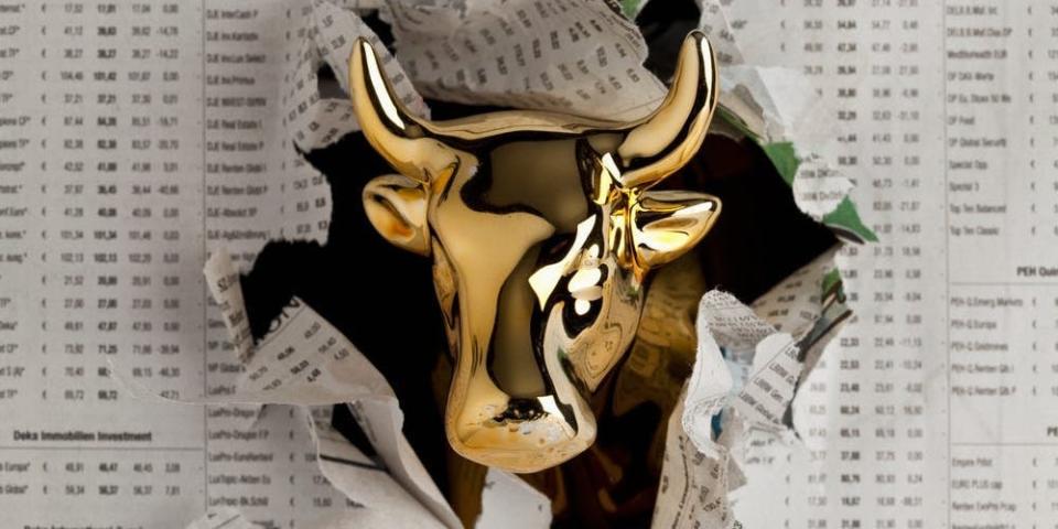 Gold bull emerging through newspaper