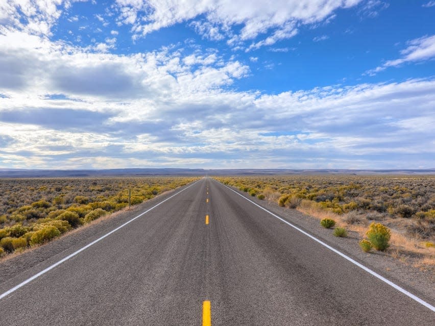 The view from an empty road in the Nevada desert. Blue sky can be seen on a cloudy day.