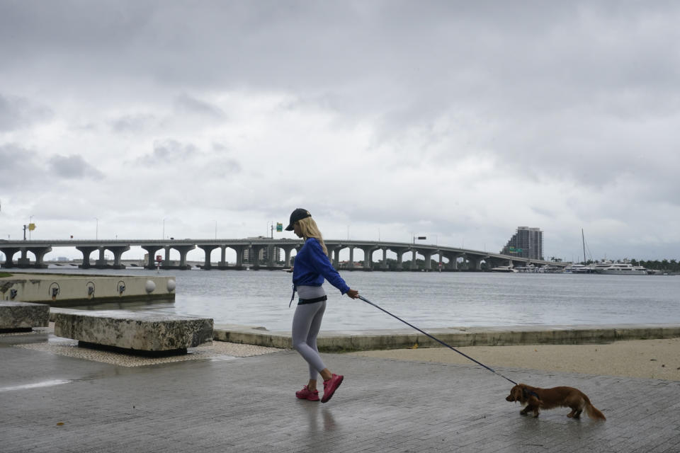 A woman walks her dog during a brief pause during a heavy downpour, Saturday, June 4, 2022, in Miami. A tropical storm warning was in effect along portions of coastal Florida and the northwestern Bahamas. Several Miami streets were flooded and authorities were towing abandoned vehicles(AP Photo/Marta Lavandier)