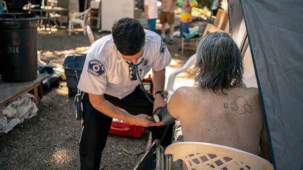 PHOTO: Gabe DeBay, Medical Services Officer with the Shoreline Fire Department, checks the blood pressure of a homeless man at a tent encampment during the hottest part of the day, July 26, 2022, in Shoreline, Wa. (David Ryder/Getty Images)