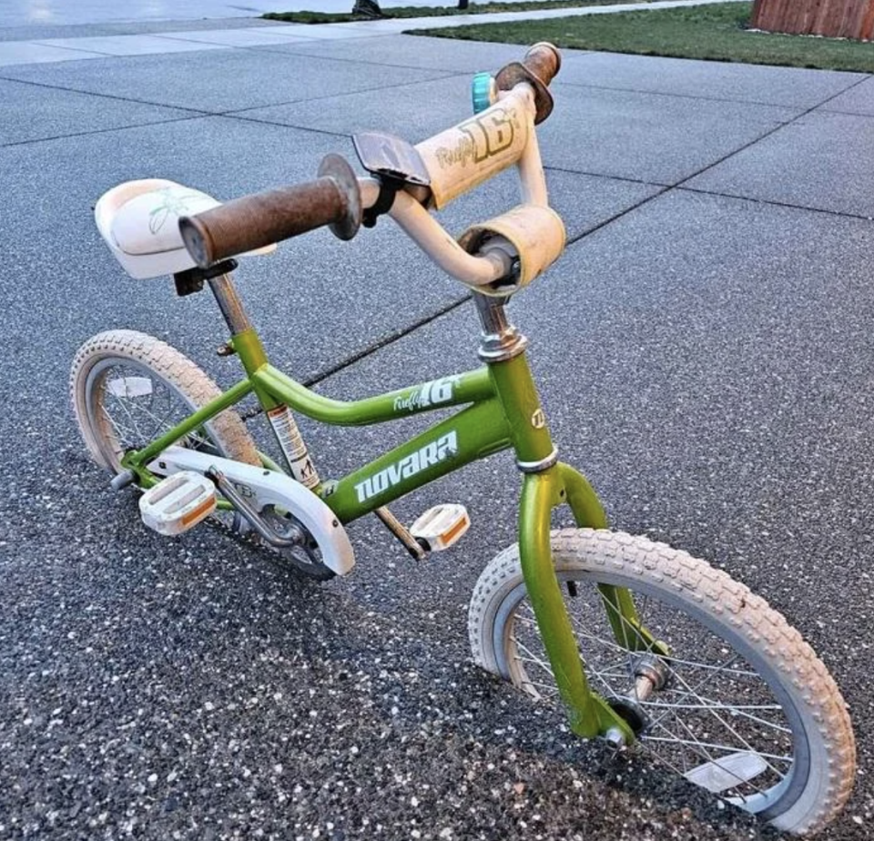 Child's green and white bicycle parked on a sidewalk