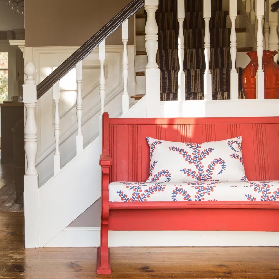 Hallway ideas with a pop of color in the form of a coral painted bench by the staircase.