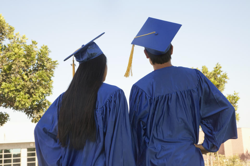 Two graduates in blue caps and gowns stand together outdoors