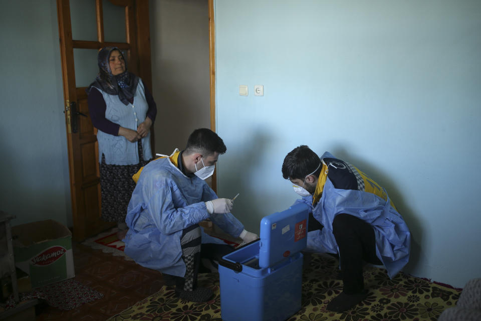 Local resident Zeynep Yigit, 70, left, looks on as Dr. Yasin Kaya, right and health worker Yusuf Duran, center of the Koyulhisar Public Health Center vaccination team, prepare a dose of the CoronaVac vaccine made by China's Sinovac Biotech Ltd., to administer to her at her house in the isolated village of Gumuslu in the district of Sivas, central Turkey, Friday, Feb. 26, 2021. (AP Photo/Emrah Gurel)