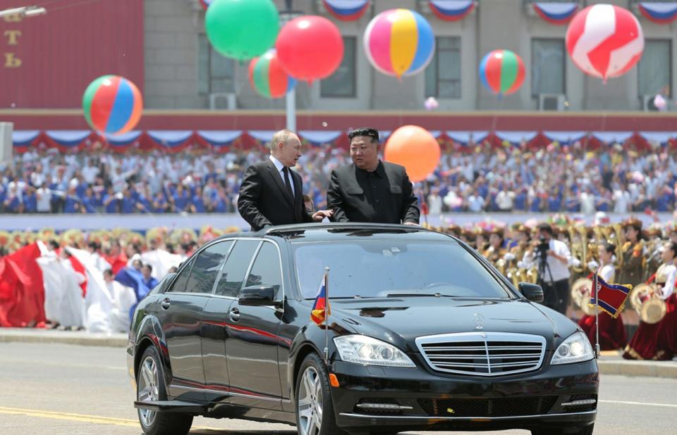 Kim Jong Un and Vladimir Putin appear from the sunroof window of a car.