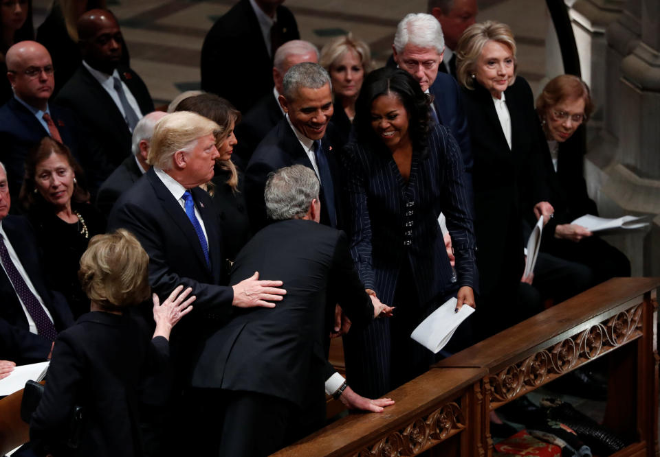 President George W. Bush reaches across in front of President Donald Trump and first lady Melania Trump to greet former President Barack Obama and former first lady Michelle Obama, sitting in the front row with former President Bill Clinton, former first lady Hillary Clinton and former first lady Rosalynn Carter as he arrives at the state funeral for his father former President George H.W. Bush at the Washington National Cathedral in Washington, D.C., Dec. 5, 2018. (Photo: Kevin Lamarque/Reuters)