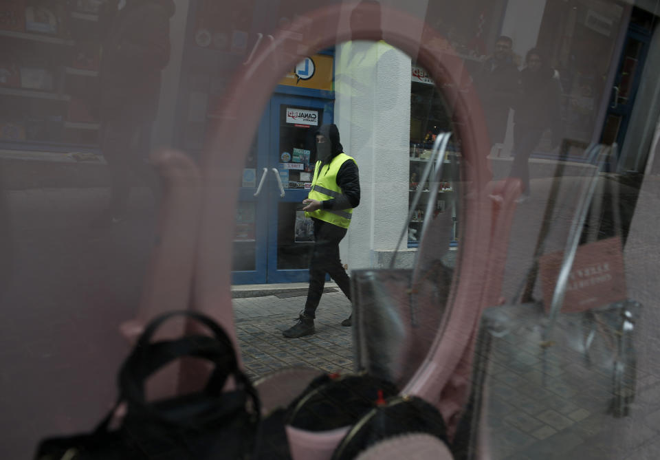 A yellow vest protestor passes a shop window in Bourges, central France, Saturday, Jan. 12, 2019. Paris brought in armored vehicles and the central French city of Bourges shuttered shops to brace for new yellow vest protests. The movement is seeking new arenas and new momentum for its weekly demonstrations. Authorities deployed 80,000 security forces nationwide for a ninth straight weekend of anti-government protests. (AP Photo/Rafael Yaghobzadeh)