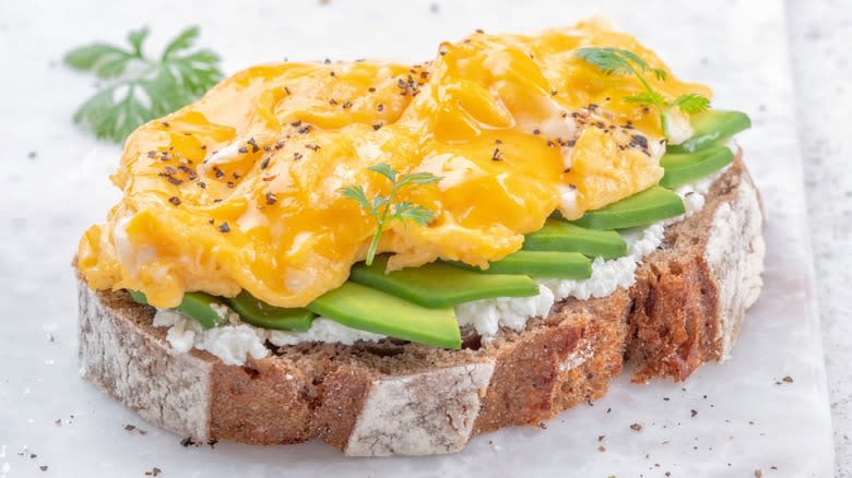 Loose scrambled eggs on avocado cheese toast with fresh herbs