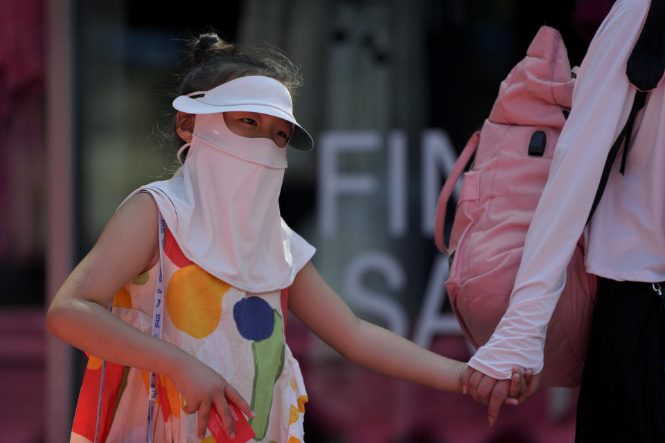 A girl wearing a sun protection face cover walks with her relative on a sweltering day at an urban waterway in Beijing, Monday, July 10, 2023. Rescuers were looking Monday for several people missing in a landslide triggered by torrential rains while employers across much of China were ordered to limit outdoor work due to scorching temperatures as the country struggled with heat, flooding and drought. (AP Photo/Andy Wong)