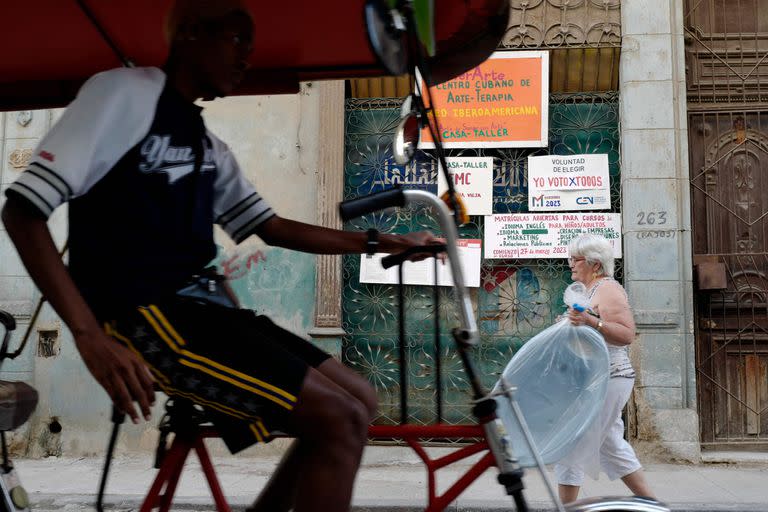 Habitantes pasan frente a pancartas que piden a los cubanos votar en las elecciones legislativas del próximo domingo, en La Habana, el 23 de marzo de 2023.