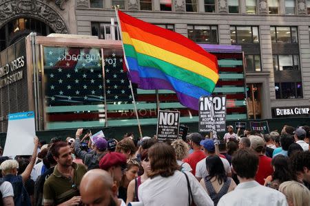 A rainbow flag flies as people protest President Donald Trump's announcement that he plans to reinstate a ban on transgender individuals from serving in any capacity in the U.S. military, in Times Square, in New York City, New York. REUTERS/Carlo Allegri
