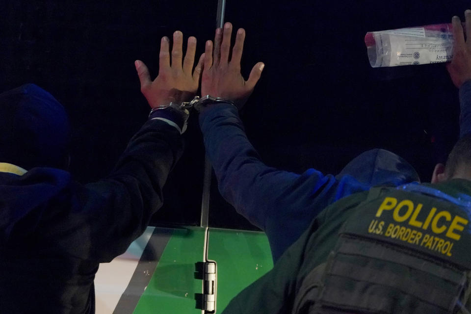 Two men are handcuffed together as a U.S. Customs and Border Protection agent pats them down before putting them in a van while taking them into custody near the U.S.-Mexico border, Saturday, March 20, 2021, in Hidalgo, Texas. (AP Photo/Julio Cortez)