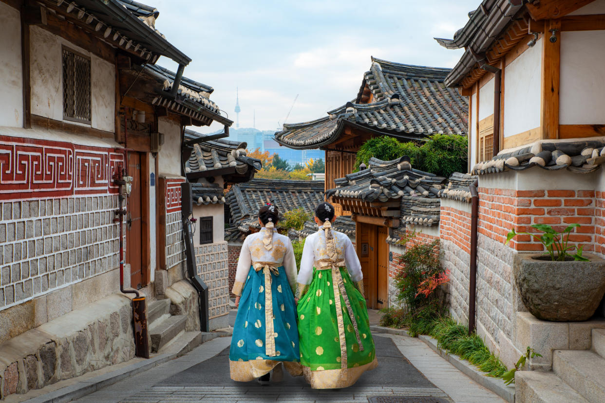 Back of two woman wearing hanbok walking through the traditional style houses of Bukchon Hanok Village in Seoul, South Korea.