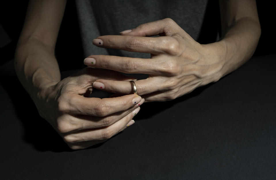 Person's hands with a ring on the left ring finger against a dark background