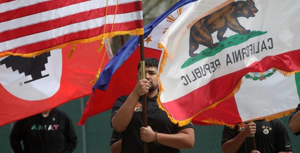 A student is overwhelmed by wind-blown flags during the Fresno State commemoration of farmworker leader César E. Chávez in the Peace Garden on March 22, 2023.