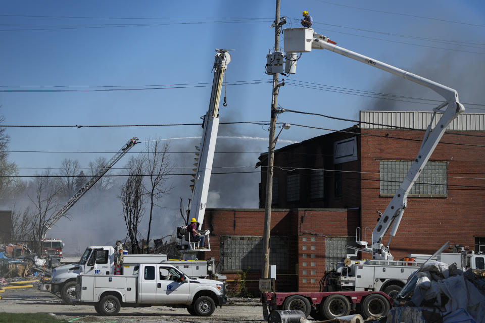 Utility workers remove utilities from the area as firefighter pour water on an industrial fire in Richmond, Ind., Wednesday, April 12, 2023. Authorities urged people to evacuate if they live near the fire. The former factory site was used to store plastics and other materials for recycling or resale. (AP Photo/Michael Conroy)