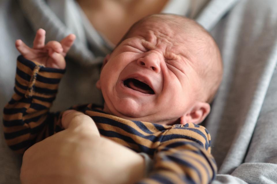 Crying infant being held, expressing discomfort or need, possibly signaling common parenting challenges