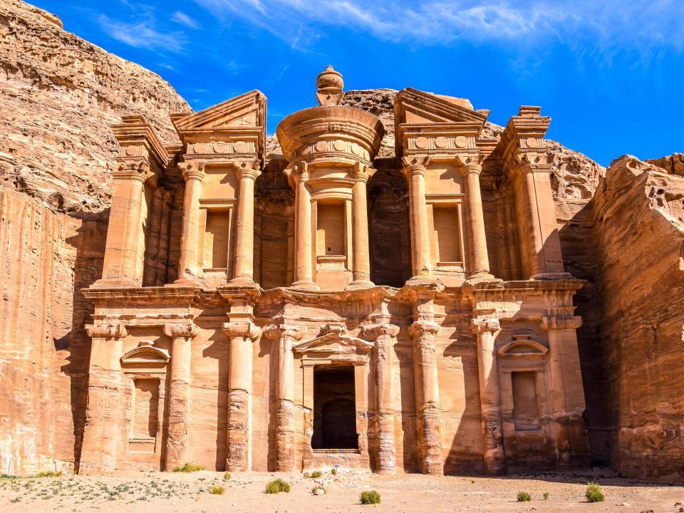 A view of Petra, a city carved into sandstone cliffs, with blue skies
