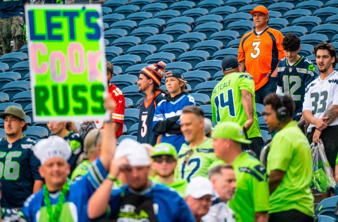A fan wearing a Russell Wilson jersey stands behind a Seahawks fan holding a sign that reads, “Let’s Cook Russ,” before the start of an NFL game on Monday, Sept. 12, 2022, at Lumen Field in Seattle.