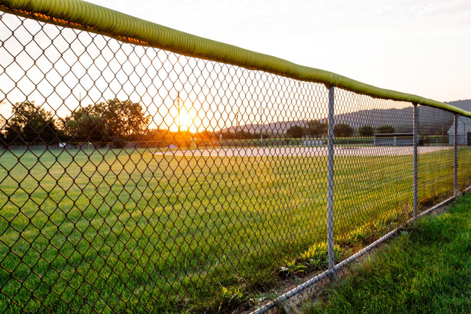 Empty baseball field, school sports field with chainlink fence at high school or public park in rural small town America. Nostalgia concept for junior high school sports team, physical education, or community sport recreation center. No people, copy space in sky during day during sunset.