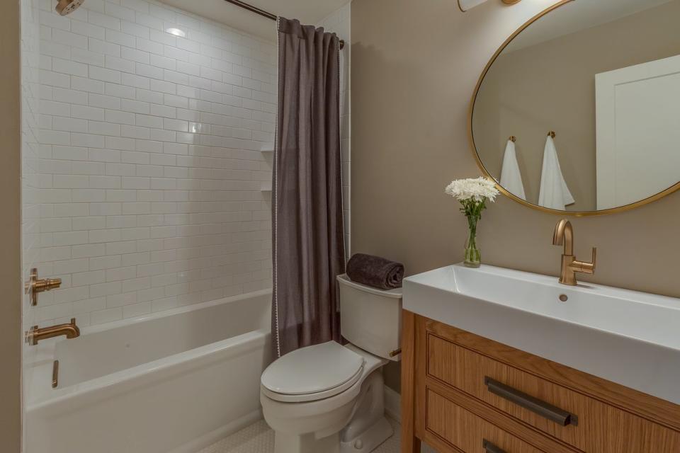 A full bathroom with a white shower and tub combo and a circular gold mirror. 